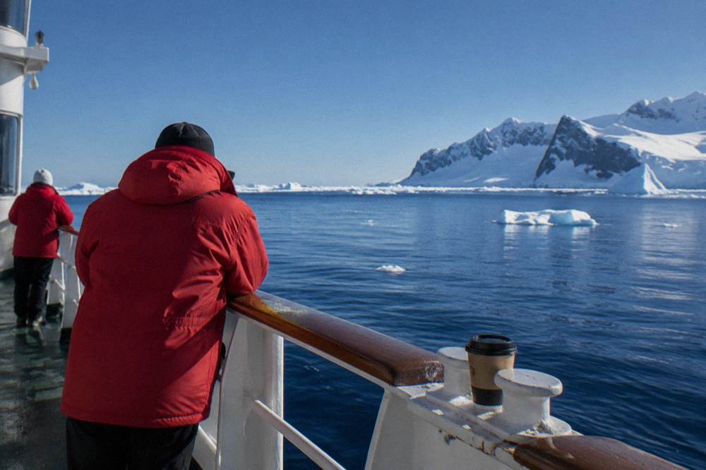 Passengers in red expedition parkas standing along a ship rail watching calm polar water