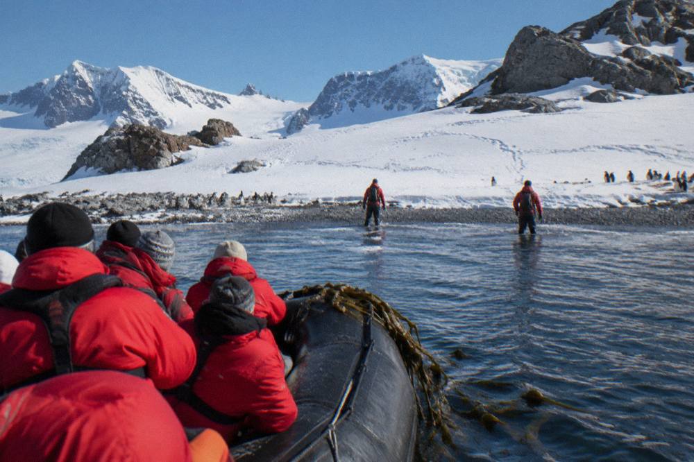 A Zodiac boat carrying passengers toward a snowy Antarctic beach where expedition staff wait