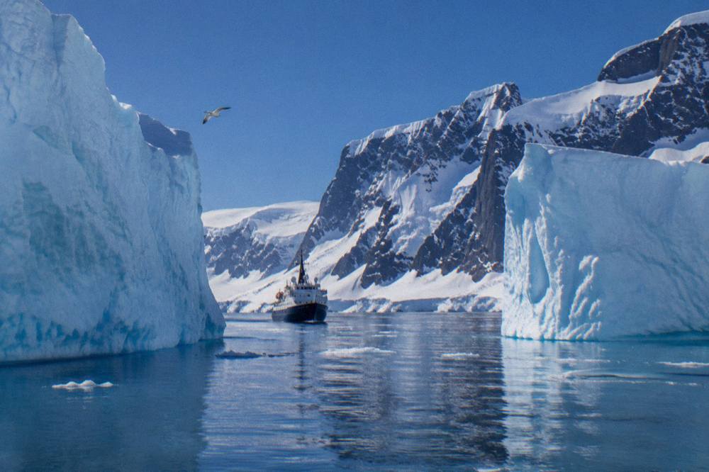 A small expedition ship moving through calm polar water between icebergs