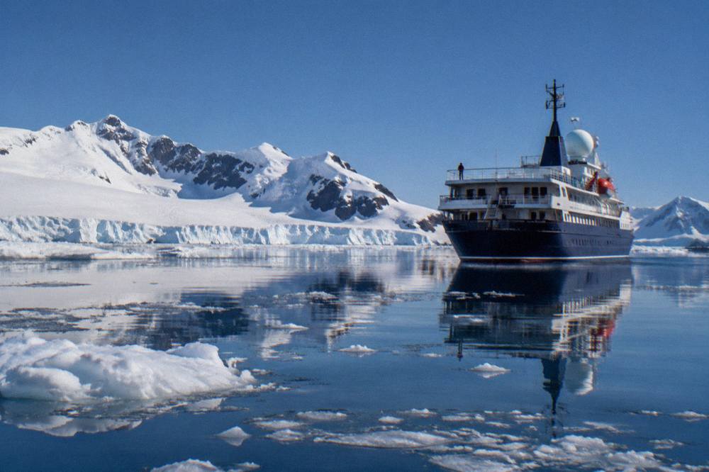 Expedition ship anchored in a calm Antarctic bay surrounded by brash ice