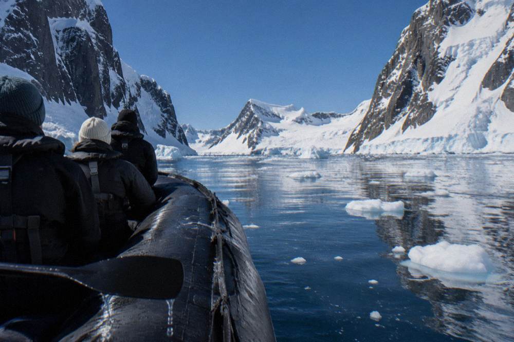 Zodiac boat with passengers in drysuits floating among small pieces of sea ice