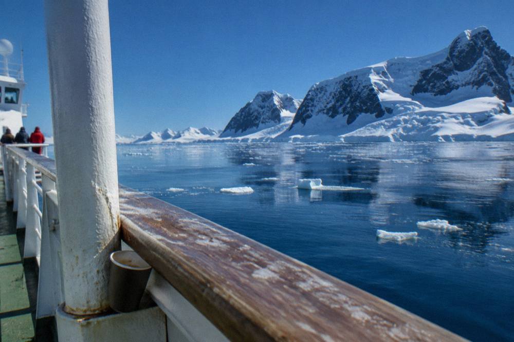 A ship deck rail above calm water dotted with brash ice