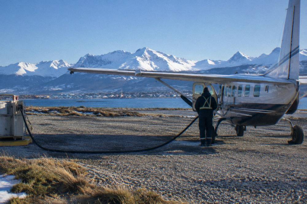 A small charter aircraft on a gravel airstrip near snowy mountains