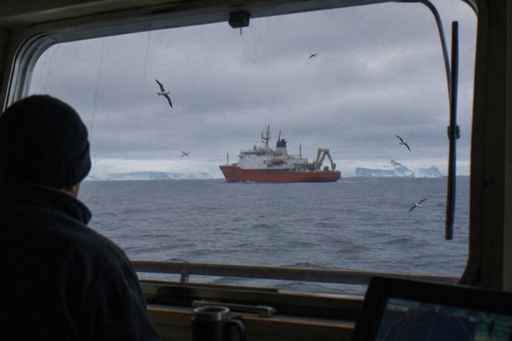 An expedition cruise ship sailing through calm polar water with icebergs on the horizon