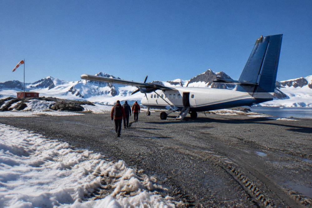 A twin-engine charter aircraft on a gravel runway beside snowy Antarctic terrain