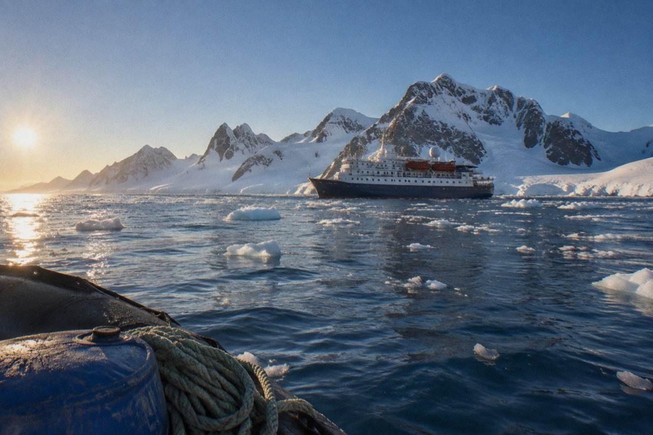A small expedition ship anchored near snowy Antarctic mountains and floating sea ice