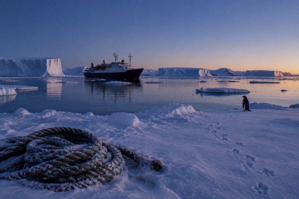 An expedition ship anchored in a calm Antarctic bay surrounded by sea ice