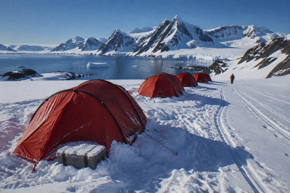 Red tents pitched on snow near a mountain range in Antarctica