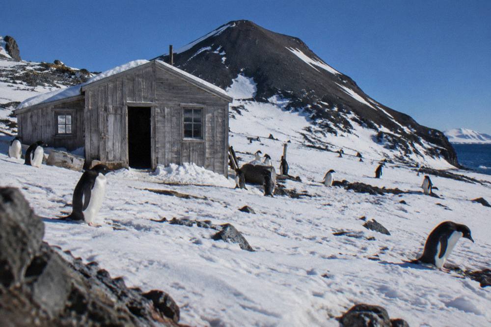 Historic wooden expedition hut surrounded by snow with dark mountains behind