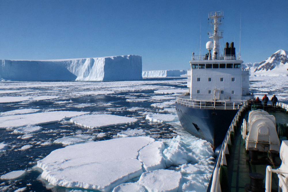Expedition ship with a reinforced bow moving through loose sea ice under low cloud
