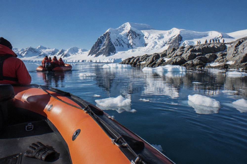 Zodiac boats near a rocky shoreline with ice floes in still water