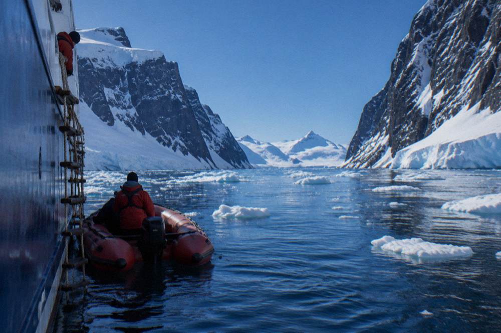 A red Zodiac floating beside an expedition ship in polar waters