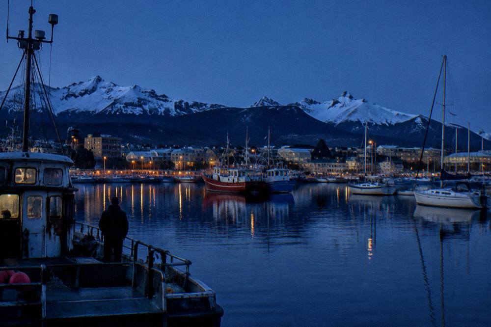 Ushuaia harbor at dusk with moored boats and mountains in the background