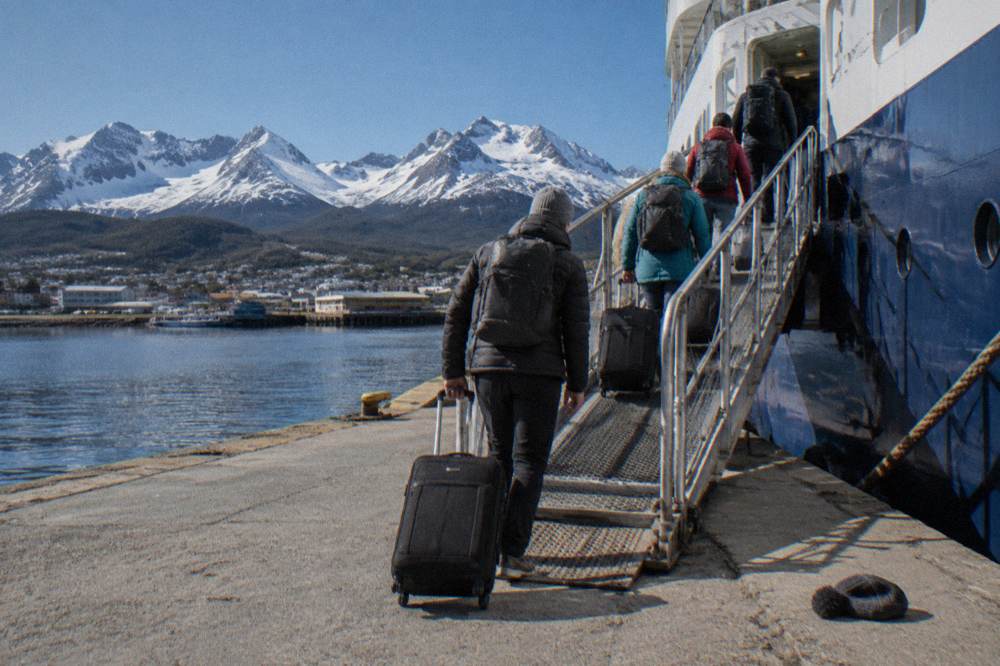 Passengers with luggage walking up the gangway of an expedition ship at the Ushuaia dock