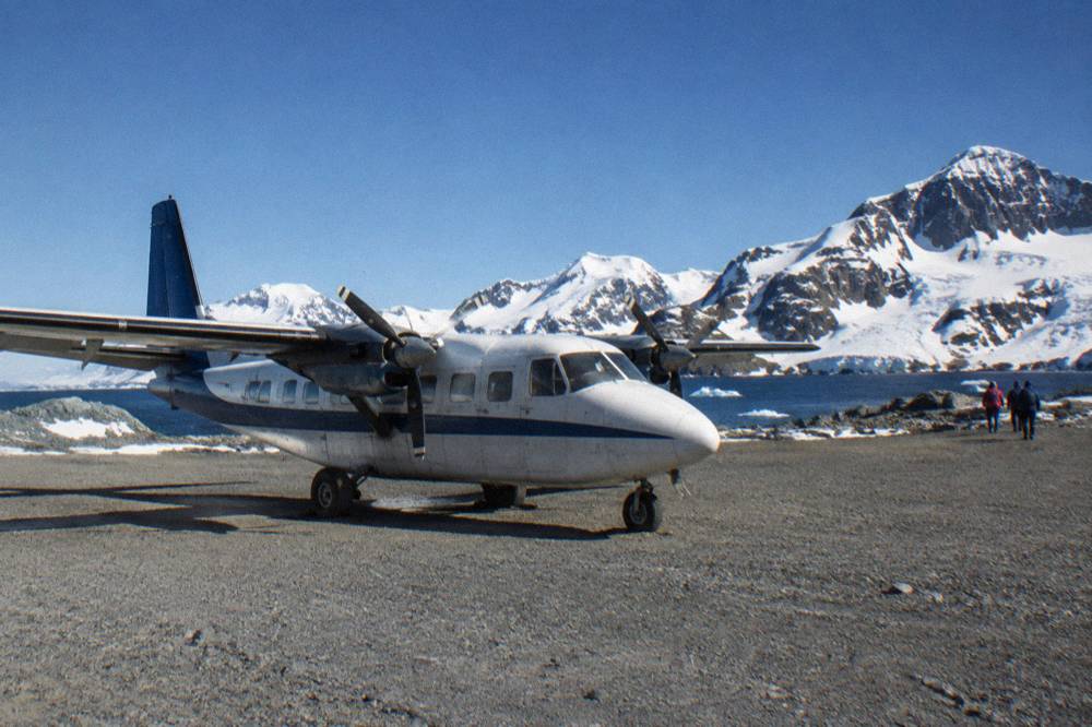 A small charter plane on a gravel runway beside a snowy island coastline