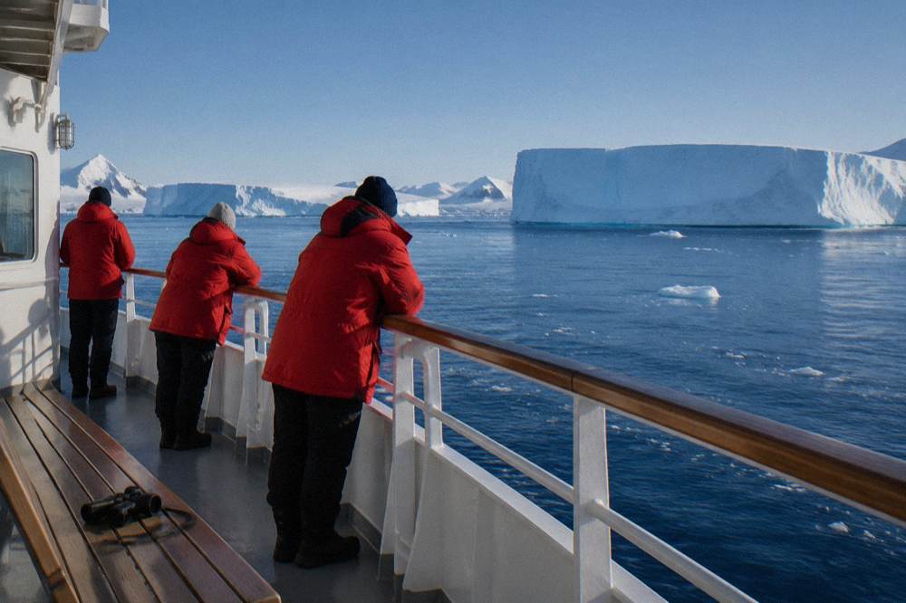 Passengers in red parkas watching icebergs from the deck of an expedition ship