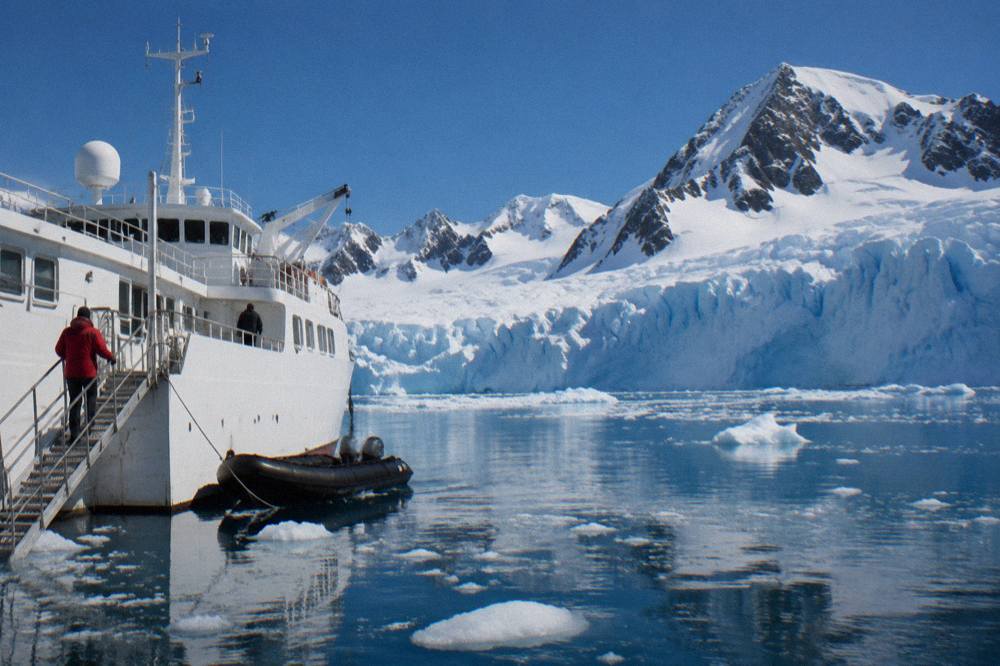 A small expedition ship moored near a glacier face in the Antarctic Peninsula