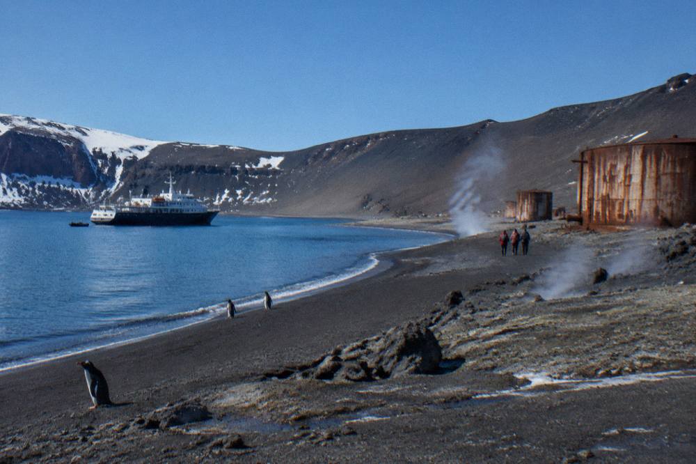 A small expedition ship anchored in a calm Antarctic bay with low clouds over dark mountains