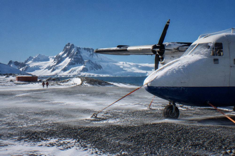 Low clouds and blowing snow over a coastal Antarctic airstrip with a parked aircraft