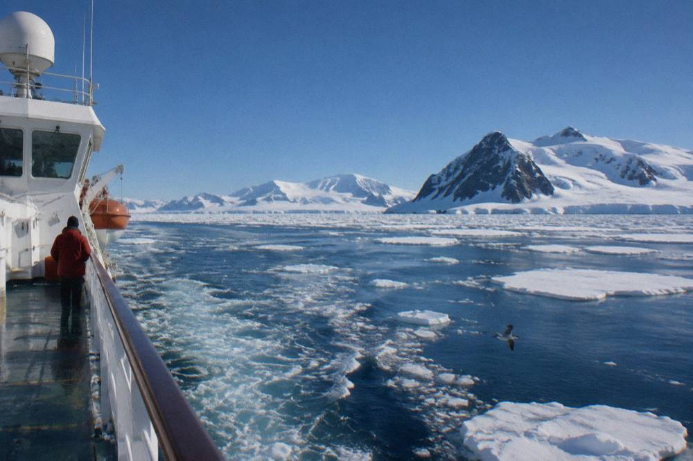 Expedition ship ploughing a wake through scattered sea ice under low clouds