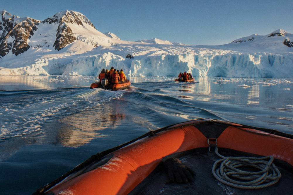 Zodiac boats approaching a glacier front in a calm Antarctic bay