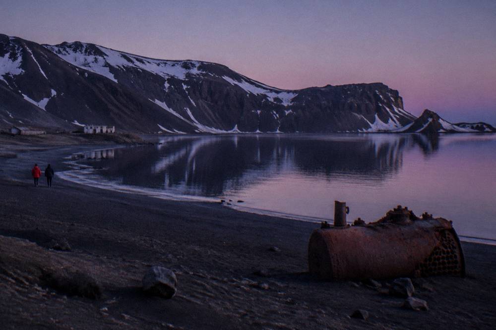Steep volcanic cliffs of Deception Island reflected in dark calm water