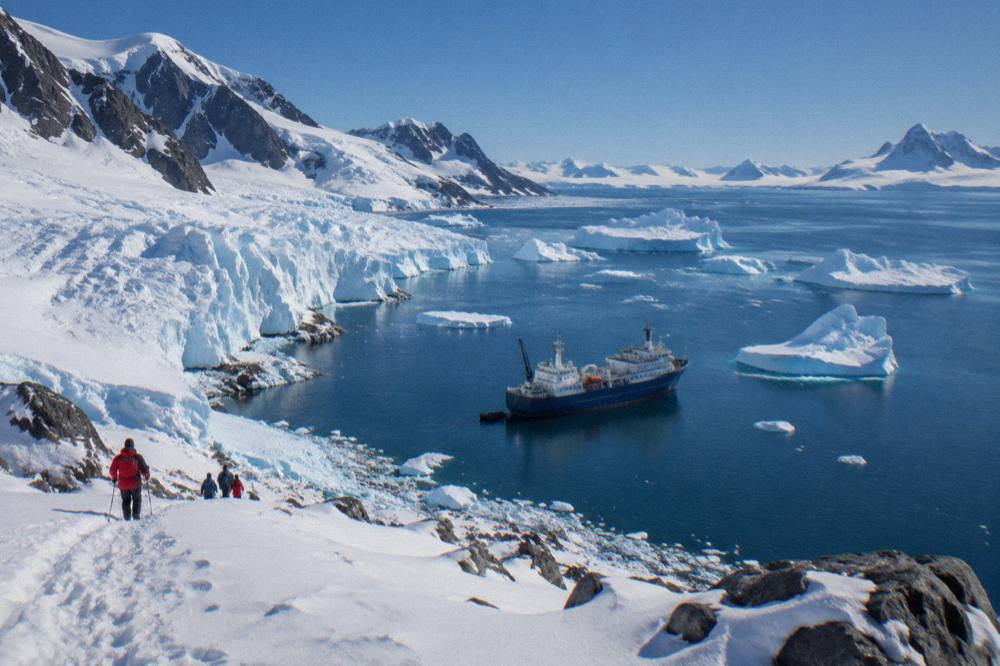 An expedition ship at anchor among blue icebergs near the Antarctic Peninsula
