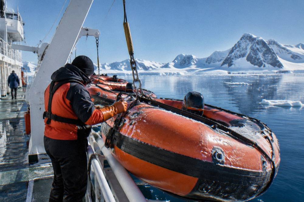 A row of orange Zodiacs lined up on a ship deck beside a crew member in expedition gear