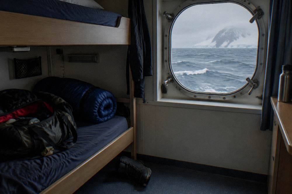 A twin expedition cabin with a porthole overlooking calm polar water