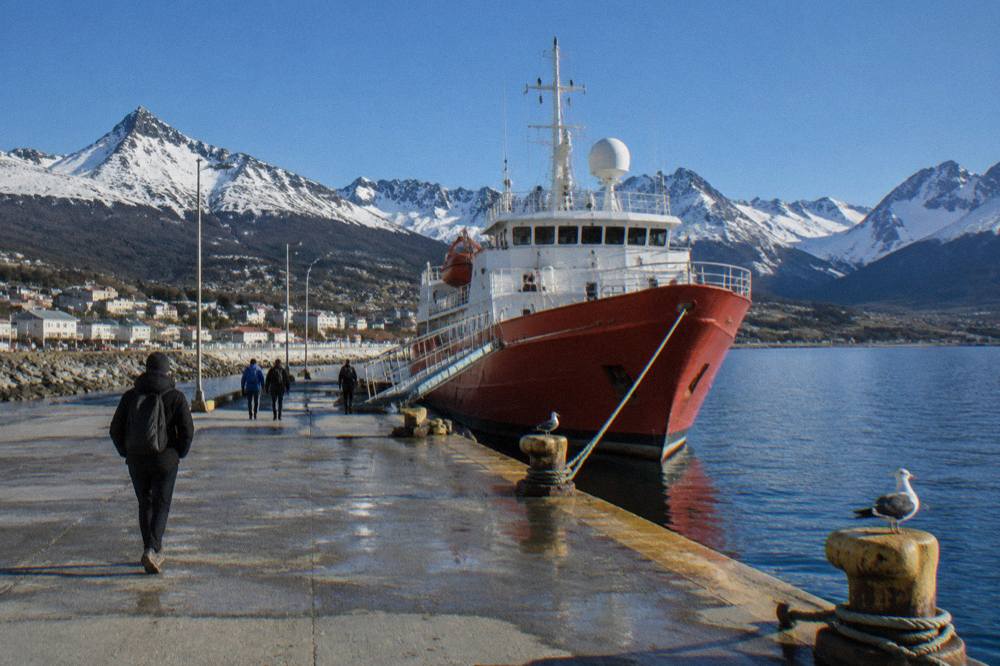 Small red-hulled expedition ship at a dock in Ushuaia with gangplank lowered