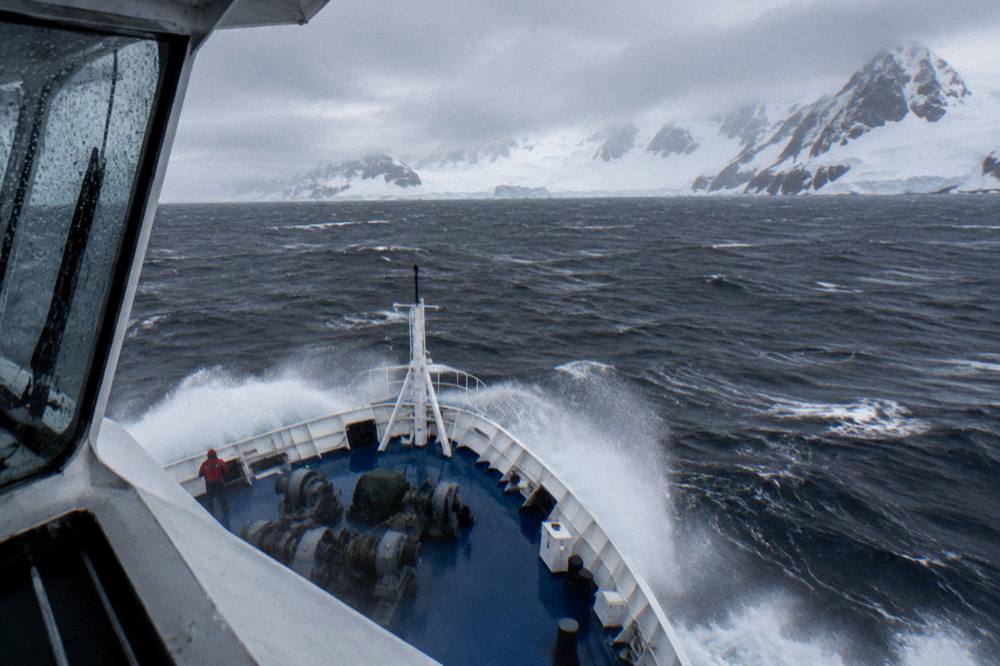 Expedition ship bow cutting through open ocean swell with white spray