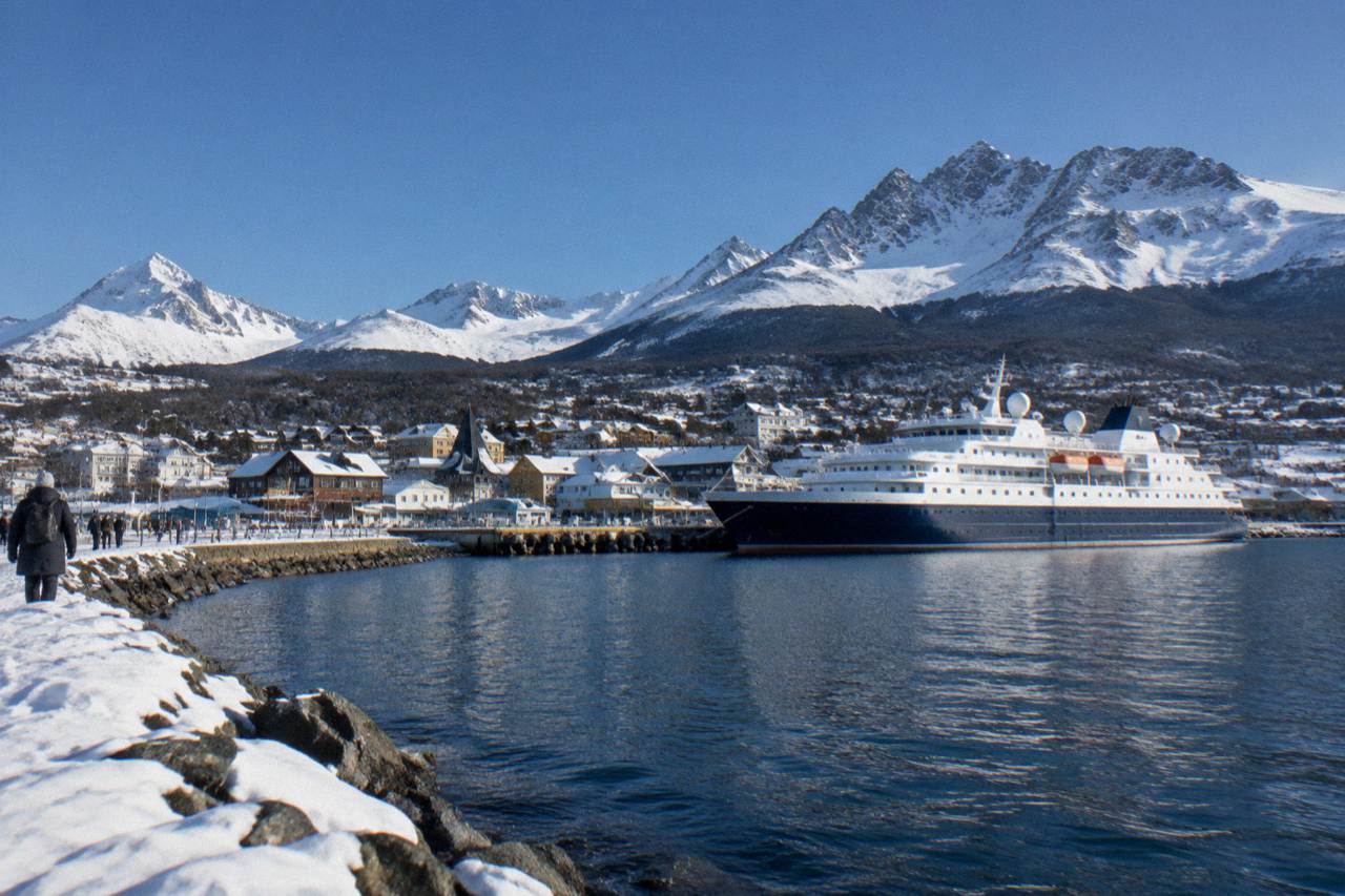 An expedition ship moored at the Ushuaia waterfront with snow-covered mountains behind the town