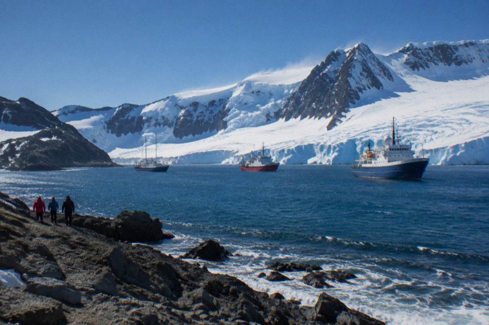 Three expedition ships of different sizes at anchor in a sheltered Antarctic bay