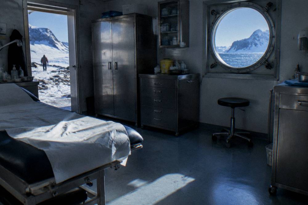 A ship's compact medical clinic room with an examination bed and supplies