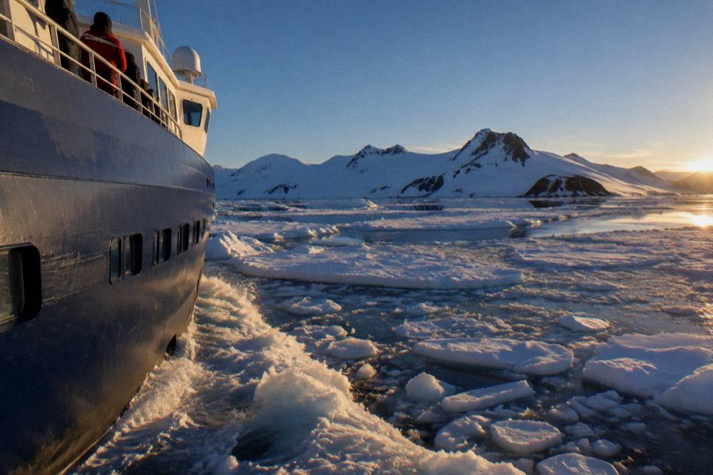 A modern expedition ship with a rounded X-Bow hull moving through light ice