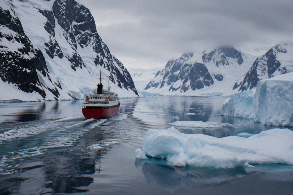 A small red expedition ship threading between icebergs in the Lemaire Channel