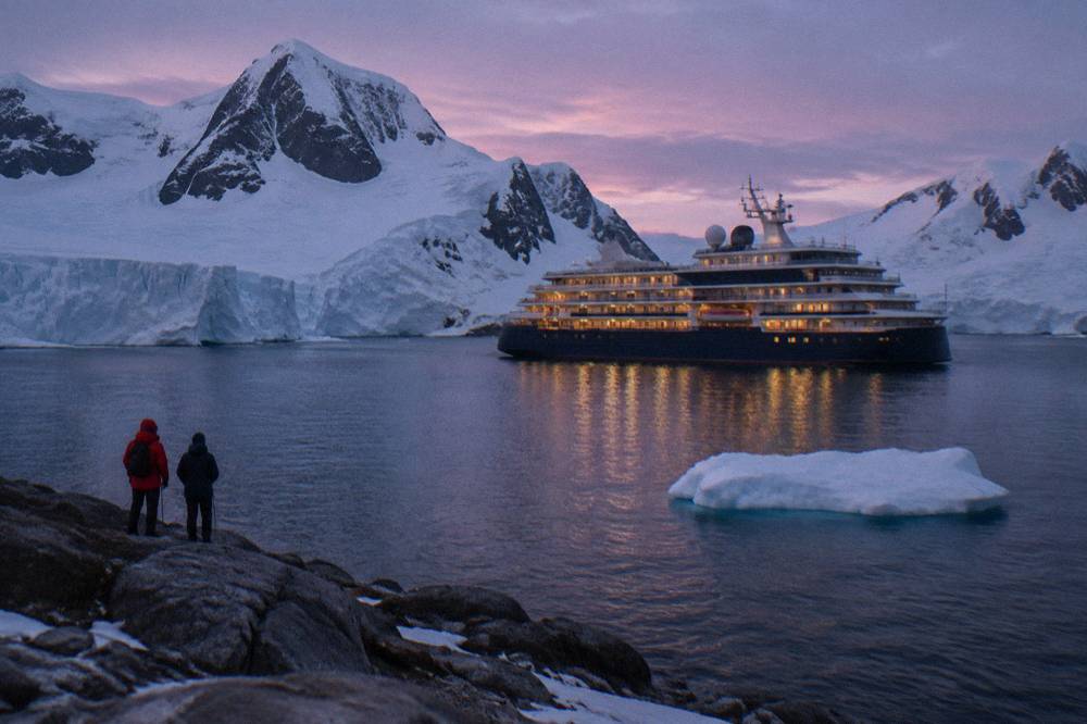 A luxury expedition ship with balconies visible along its hull in calm polar waters
