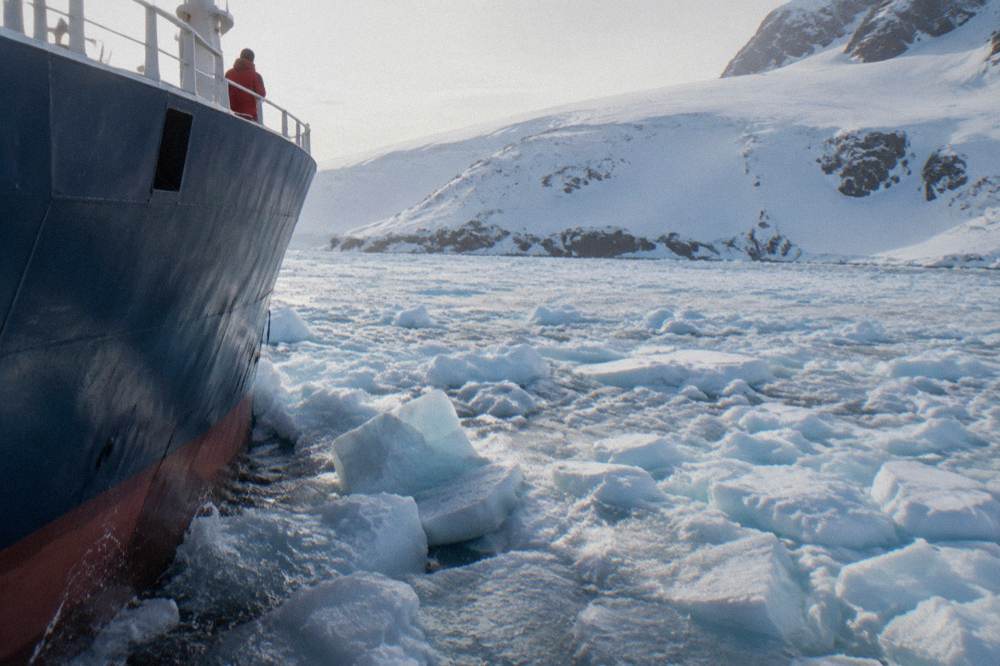 A ship's reinforced bow pushing through loose brash ice near an Antarctic shoreline