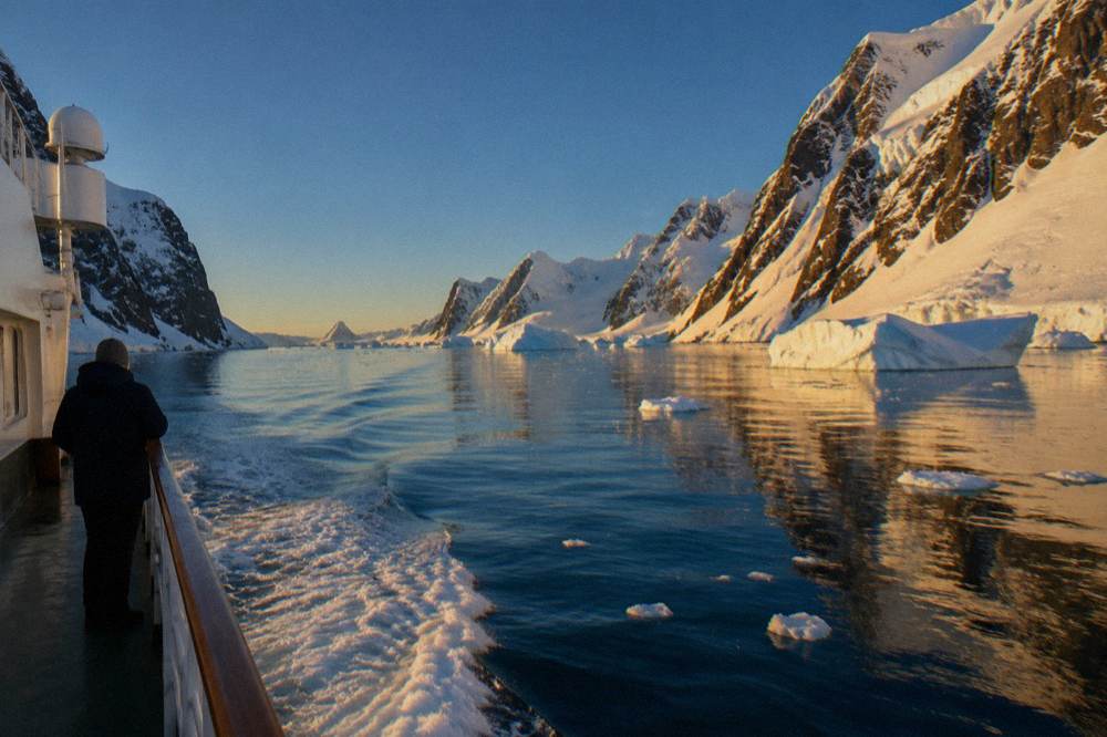 Narrow water channel between steep snow-covered cliffs with a ship wake crossing calm water