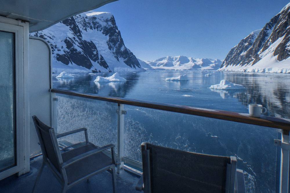 Suite balcony on an expedition ship overlooking icebergs in a still polar channel