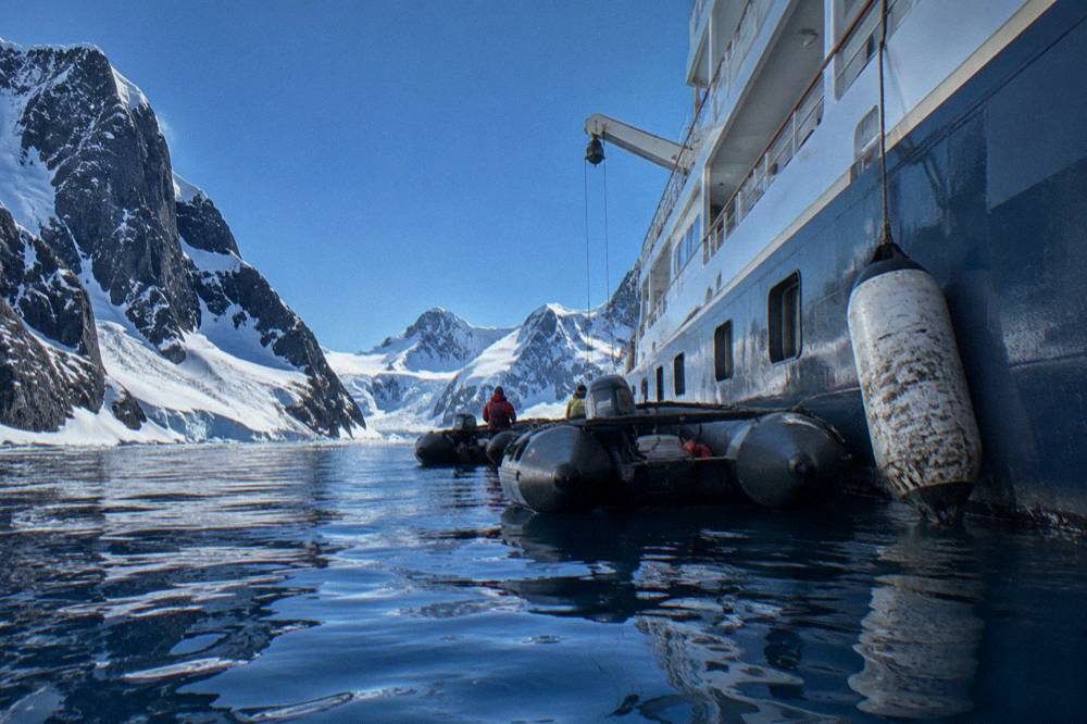 Small luxury ship moored near a glacier face with Zodiacs alongside