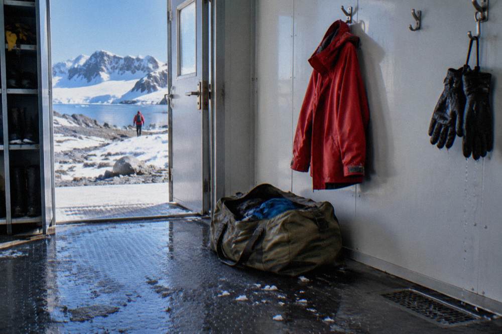 A red waterproof shell jacket hanging on a hook beside an unpacked duffel bag