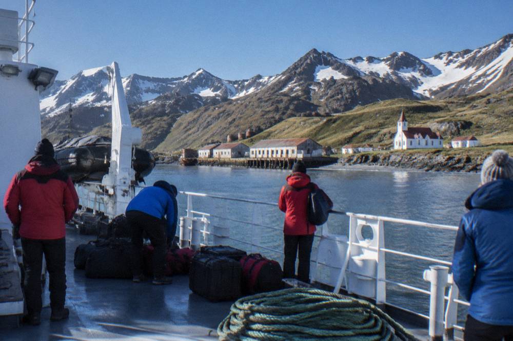 Passengers in expedition parkas preparing gear on the deck of a polar ship