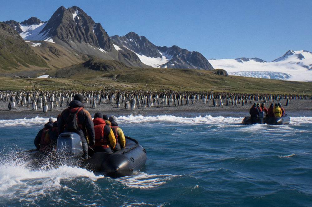 Zodiac boats carrying passengers toward a rocky Antarctic landing site