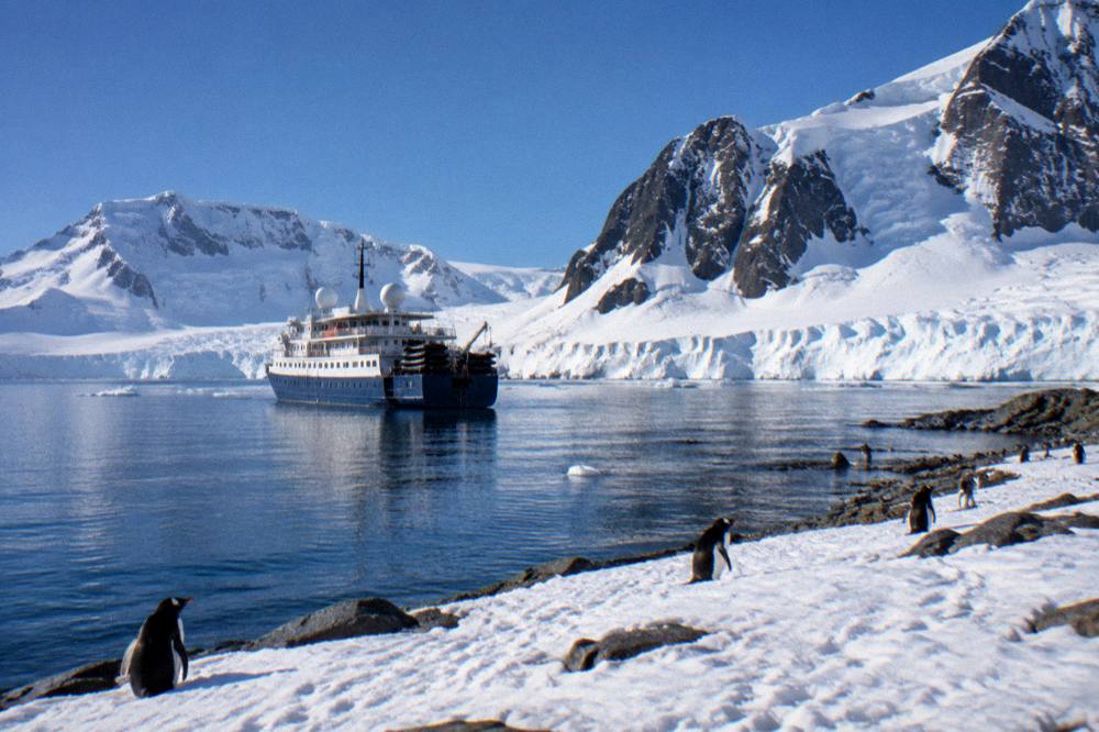 A small expedition ship at anchor near a penguin-covered Antarctic bay