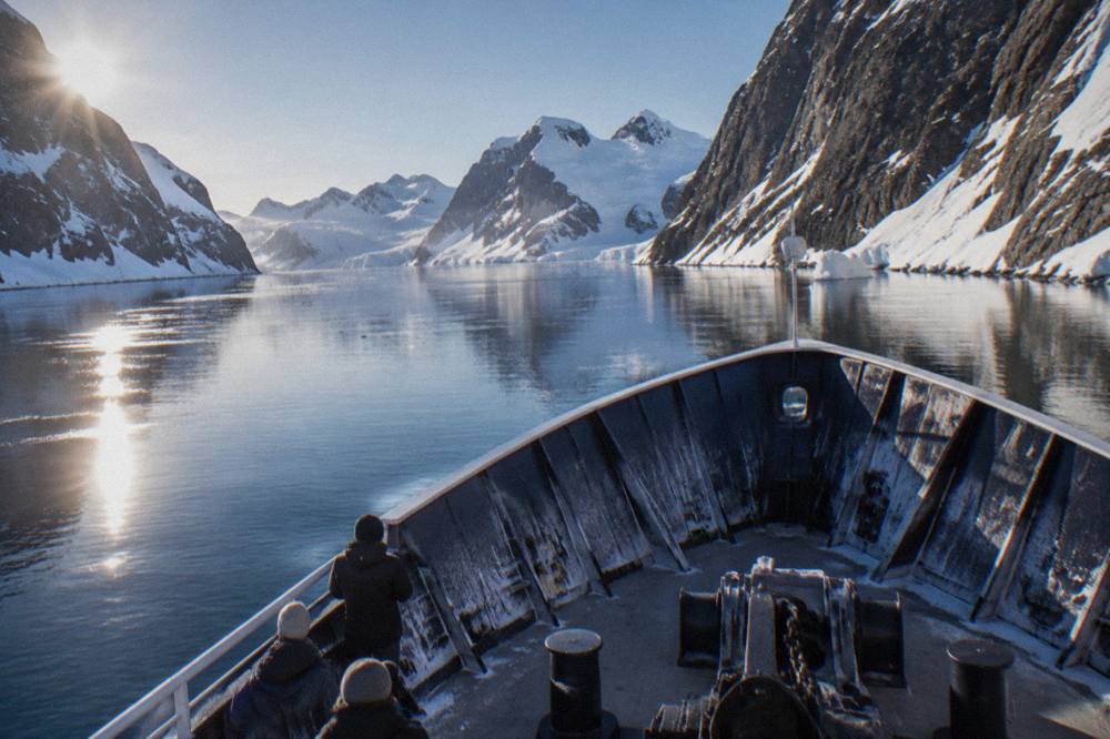 An expedition ship with an X-BOW hull cutting through calm polar water at dusk