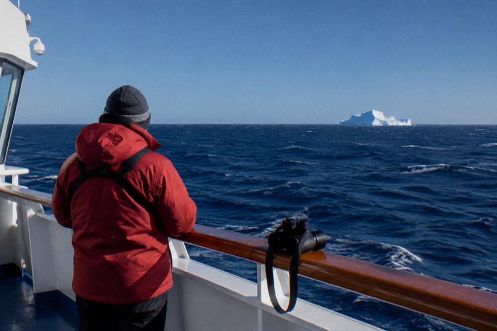 Traveller in expedition gear watching an iceberg from the observation deck of a ship