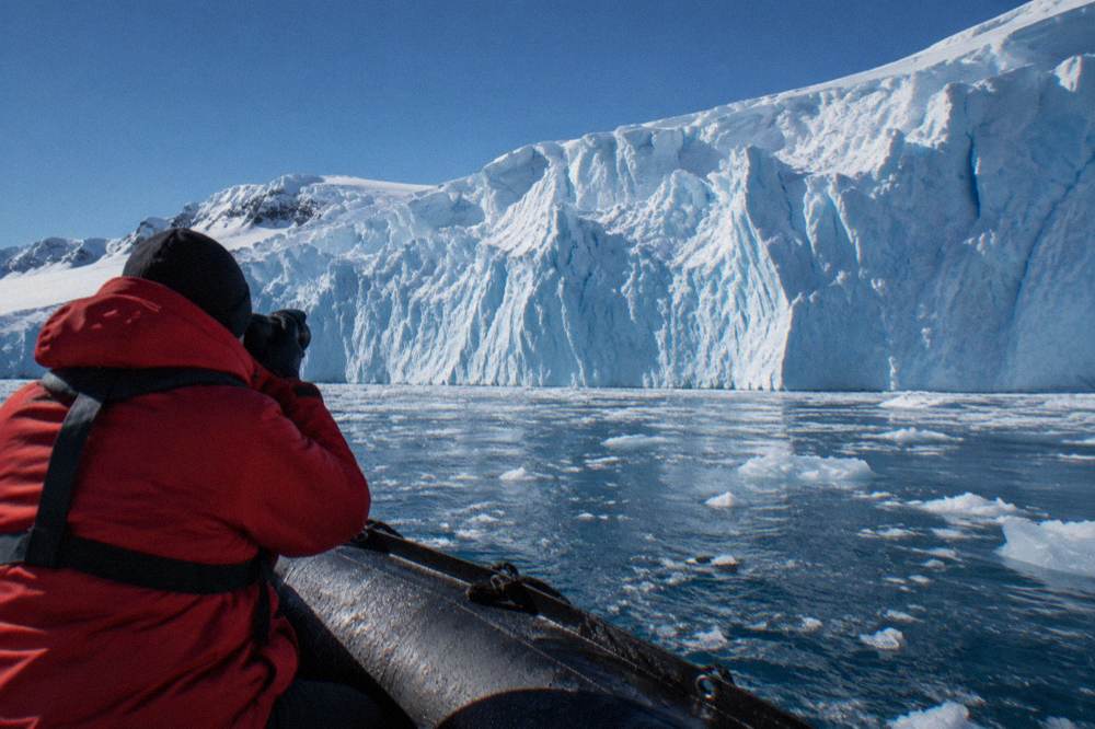 Traveller in expedition parka photographing a glacier wall from a Zodiac