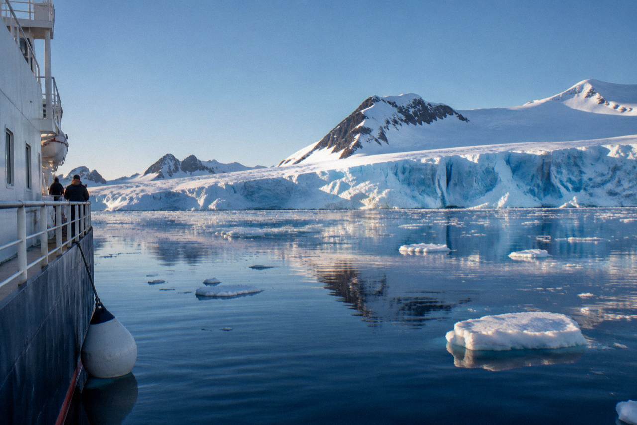 Expedition ship anchored near snow covered mountains and icebergs along the Antarctic Peninsula