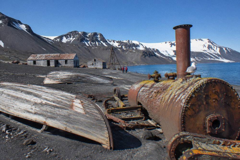 Wooden boat hulls and rusted machinery from an abandoned whaling station on a grey volcanic shore